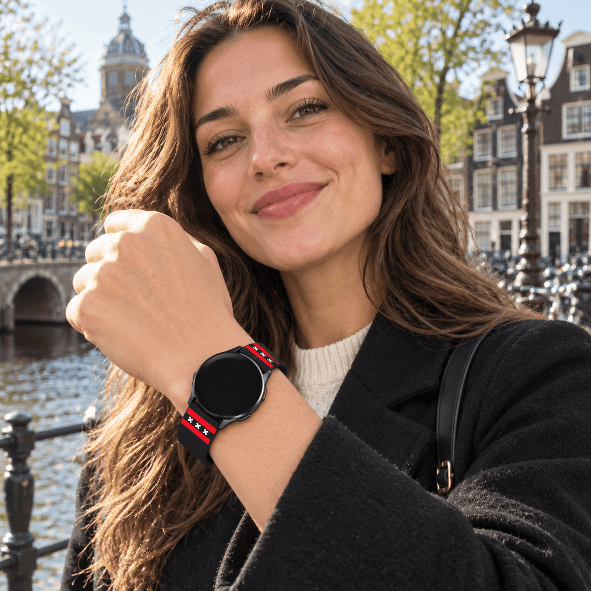 Vrouw draagt zwart-rood Amsterdam Samsung Galaxy horlogebandje met drie witte Andreaskruisen aan de Amsterdamse grachten.