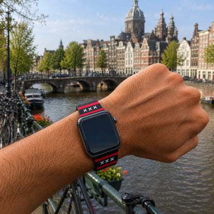 Amsterdam Apple Watch bandje van BNationX met zwarte band, rode strepen en witte Andreaskruizen, gedragen aan de Amsterdamse grachten. Silicone smartwatch band geïnspireerd op de vlag van Amsterdam.
